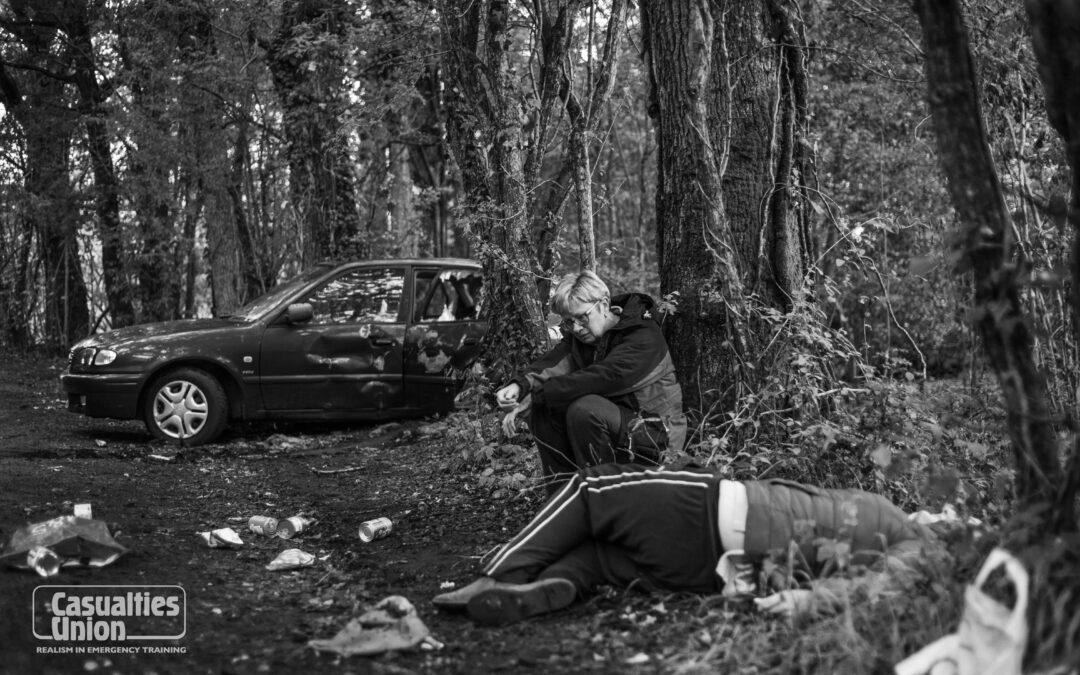A woman sits by a tree whilst another lady is lying on the floor during a staged vehicle collision incident for emergency services training