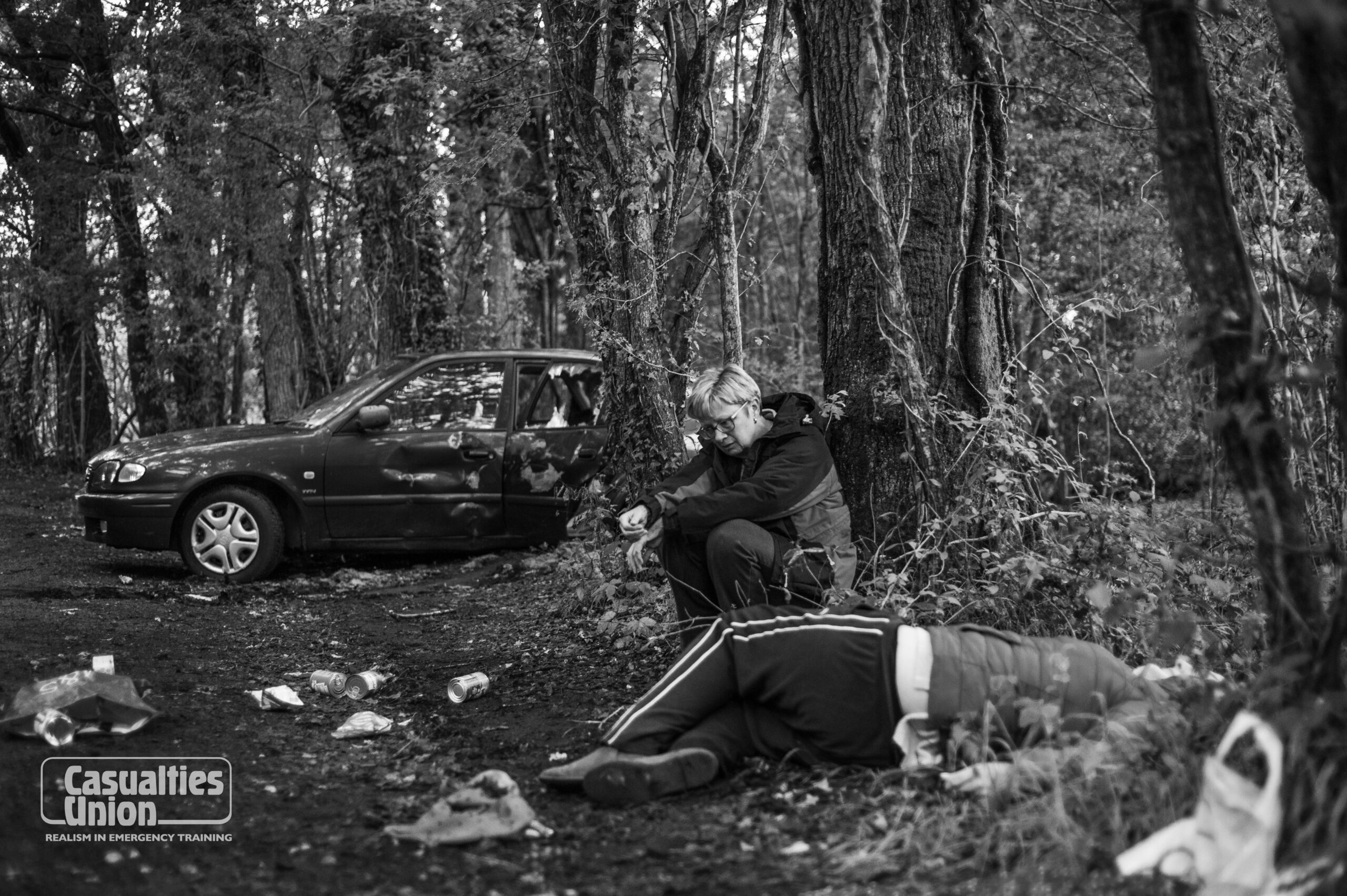 A woman sits by a tree whilst another lady is lying on the floor during a staged vehicle collision incident for emergency services training