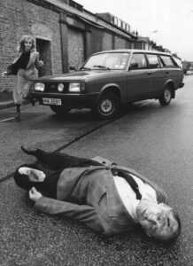 A simulated car incident scenario where a man has been hit by a car. A woman is seen running towards the casualty portrayed by a Casualties Union volunteer