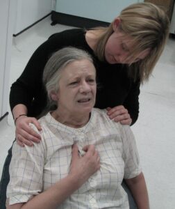 A woman portraying an individual having a heart attack using casualty simulation skills.